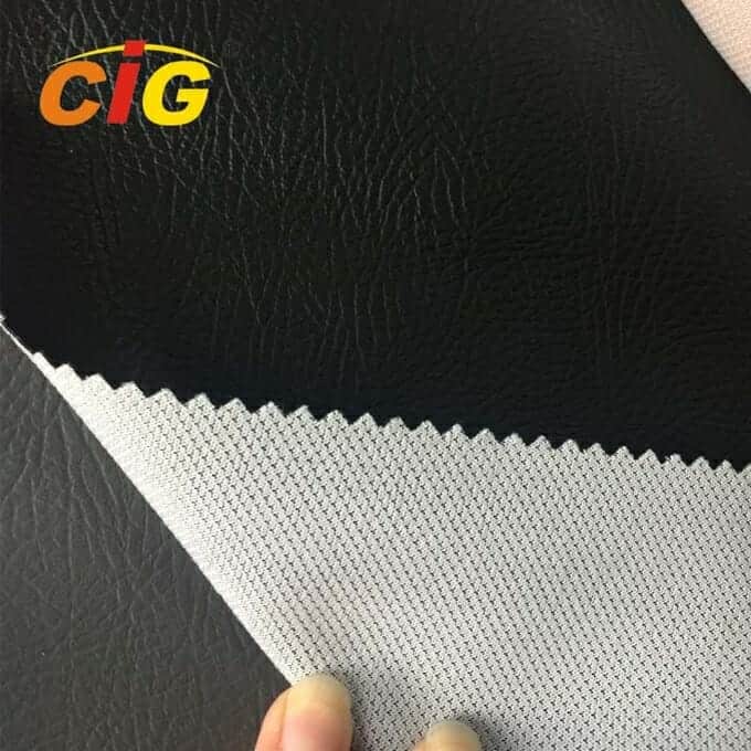 Una vista de primer plano de una mano que sostiene una muestra de cuero sintético negro con un respaldo de tela blanca, que muestra detalles de textura.