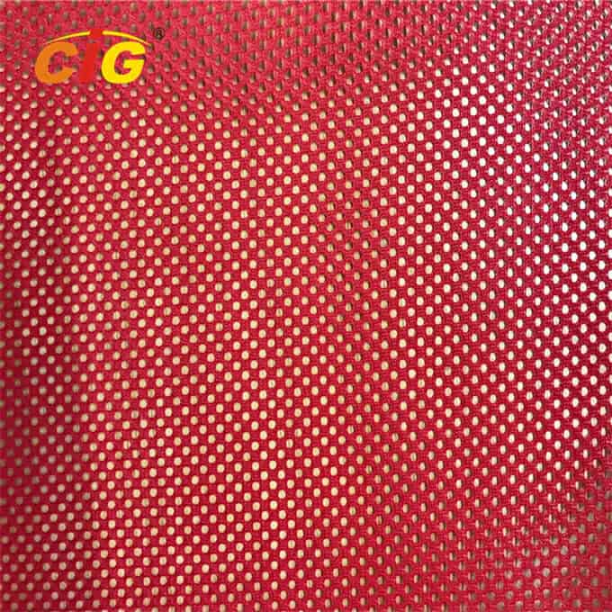 Primer plano de tela roja con puntos dorados metálicos y un logo "cg" dorado en la esquina superior izquierda.
