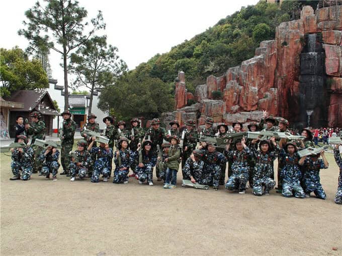 Eine Gruppe von Menschen in Militäruniformen posiert mit Gewehren vor einer felsigen Kulisse.