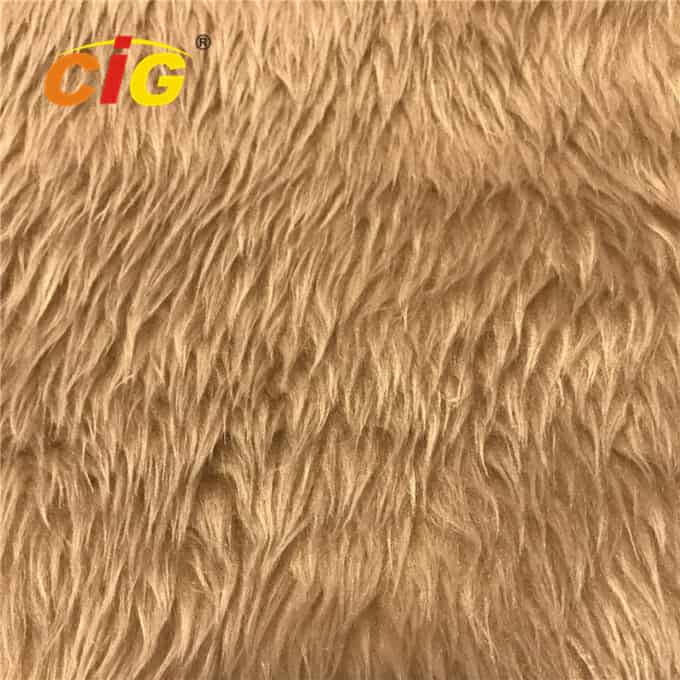Close-up of a textured beige faux fur fabric with wavy patterns, branded with a small orange "cig®" logo in the top right corner.