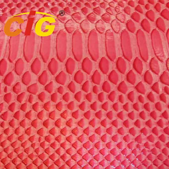 Slika od blizu rdečega, teksturiranega materiala z vzorcem krokodilje kože s črkama "cig" in simbolom registrirane blagovne znamke v rumeni barvi v zgornjem levem kotu.