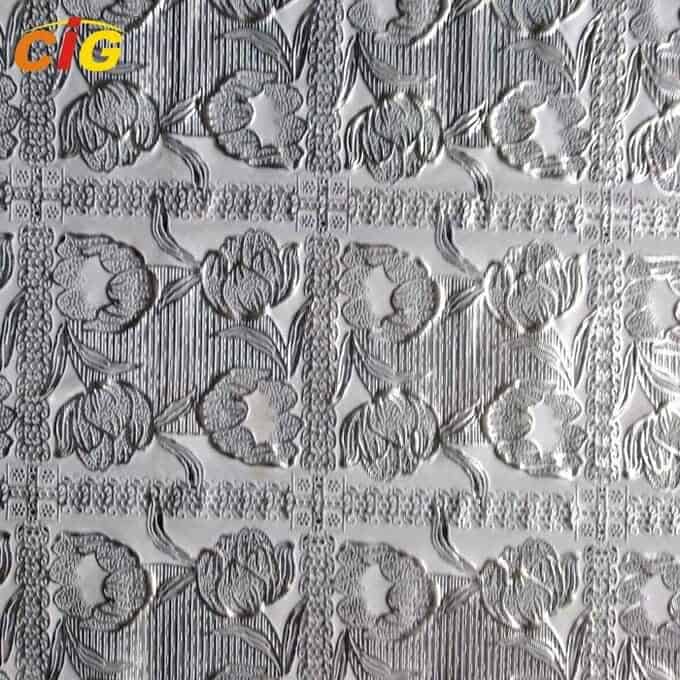Chapa metálica estampada con diseños florales y rombos en relieve en tonos plata y grises.