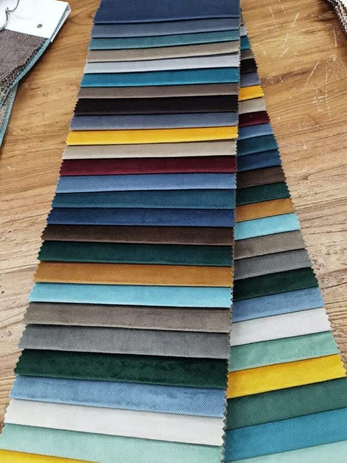 Wybór kolorowych próbek tkanin ułożonych w rzędzie na drewnianym stole, przedstawiających różnorodne kolory i tekstury.