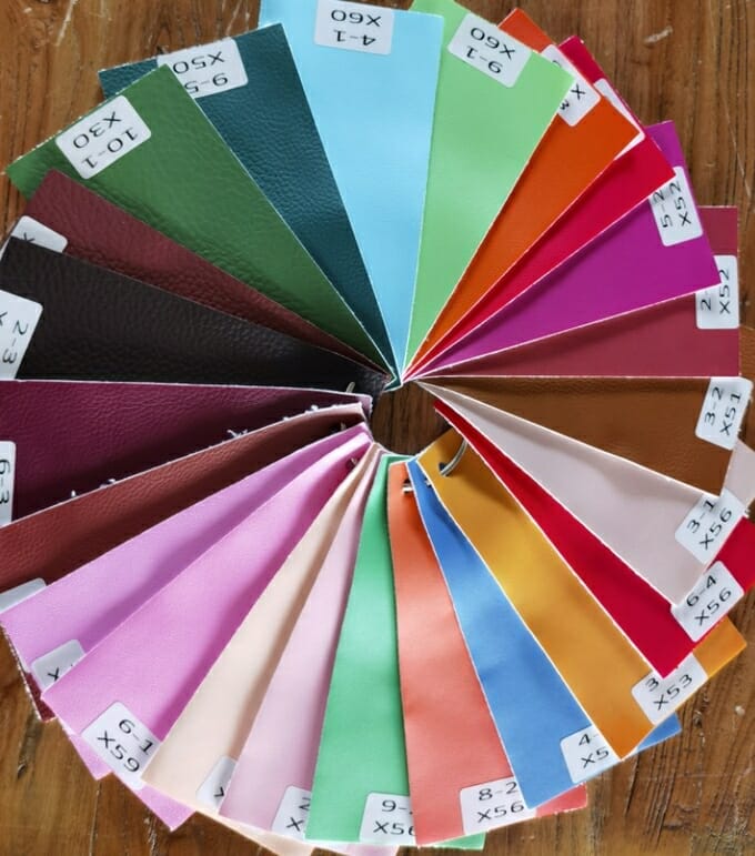 Colorful fabric swatches arranged in a circular pattern on a wooden surface, each labeled with a code.