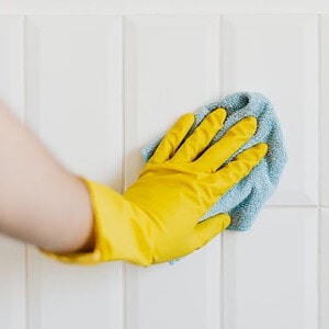 Person wearing yellow gloves cleaning white wall panels with a cloth, demonstrating proper maintenance and care for wall surfaces.