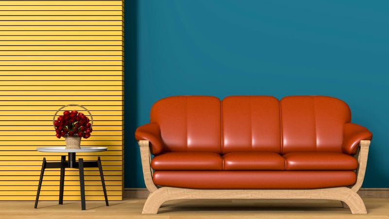 Modern orange sofa with wooden frame against a vibrant blue wall and a yellow textured wall panel, showcasing stylish interior decor options for home enhancement.
