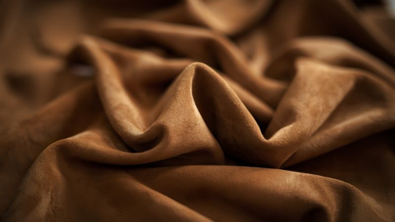 Närbild av mjukt, brunt mockatyg som framhäver dess textur och flexibilitet.