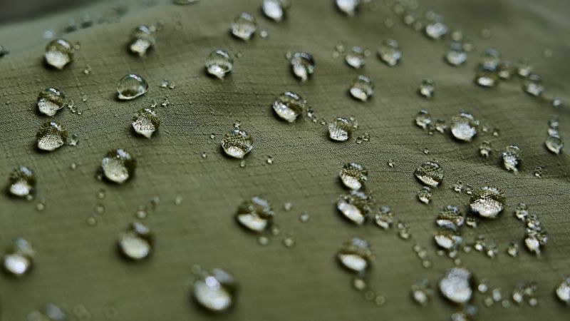 Waterproof fabric with water droplets demonstrating water resistance and protection against moisture. Ideal for outdoor gear, clothing, and upholstery to keep items dry and protected from water damage.
